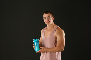 Athletic young man with protein shake on black background