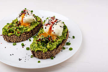 Poached eggs with avocado guacomole on brown bread with sesame seeds. Healthy breakfast on a white background.