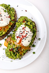 Poached eggs with avocado guacomole on brown bread with sesame seeds. Healthy breakfast on a white background.