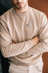 cropped view of bearded man standing with crossed arms on brown
