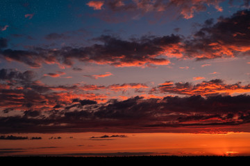 Evening sky at sunset background. Dark clouds hanging above horizon. Majestic cloudscape in blue, orange, violet shades. Grey cloudlets bringing rain. Countryside skyline in twilight time