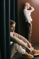 blonde woman in white blouse and pensive bearded man sitting near curtain