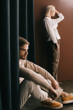 Blonde Woman In White Blouse And Pensive Bearded Man Sitting Near Curtain