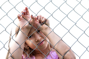 Sad girl behind metal wire mesh fence. Abandoned upset and lonely child outdoor. Depressed preteen...