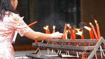 Video 4k of hand holding flame from burning red chinese candle in the temple