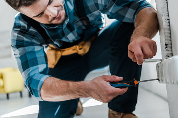 bearded repairman in uniform sitting while fixing power socket with screwdriver