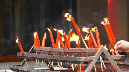 Video 4k of hand holding flame from burning red chinese candle in the temple