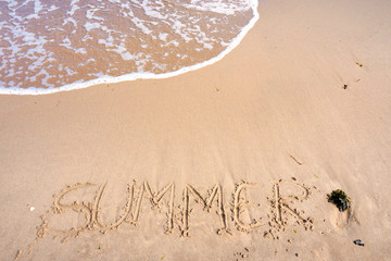 The word "summer" written in the sand on a beach