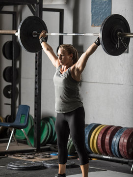 Strong female weight lifter with barbell over her head.
