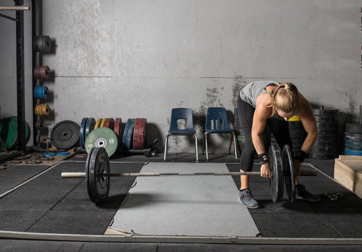 Young female power lifter loading weights onto barbell