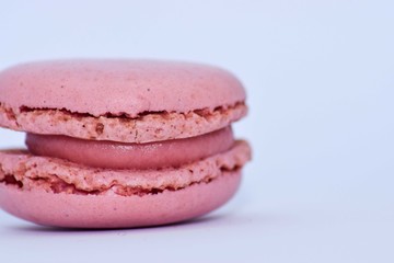 Side close up of a pink macaroon with pink filling on white background
