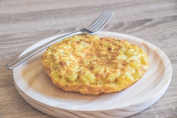 Spanish tortilla on a wood plate with a fork on the side