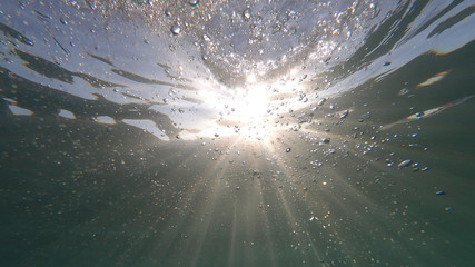 Underwater bubbles with sunlight through water surface as seen in natural scene at Caribbean turquoise open ocean sea