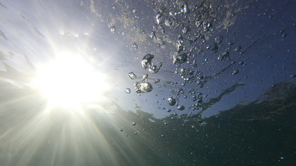 Underwater bubbles with sunlight through water surface as seen in natural scene at Caribbean turquoise open ocean sea