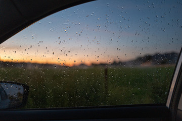 Water droplets on a car window at sunset near a rural field