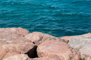 ordinary stone shoreline with blue water wavy surface background 