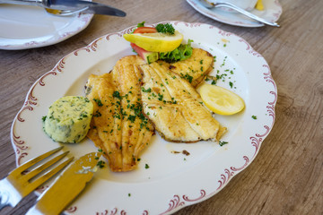 fried plaice fillet with herb butter and lemon on a plate on a wooden table, typical food in northern germany at the coast, selected focus, narrow depth of field