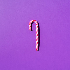 Christmas candy cane on violet background with copy space. Top view. Greeting card on Christmas and New Year. Minimal festive concept