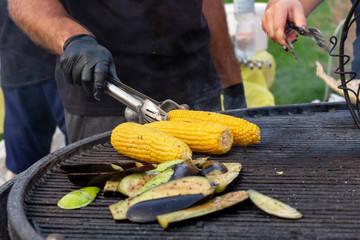 A cook fries corn and vegetables on a charcoal grill. Food and cooking equipment at a street food festival