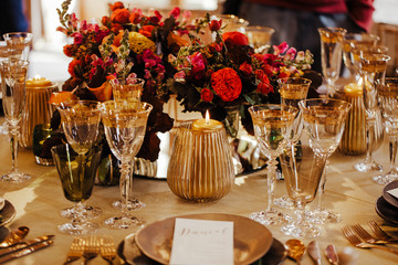 Table set for an event party or wedding reception. Beautiful flowers and glassware set on the table. Selective focus on flowers. Warm colours.