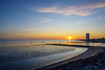 beach and skyscraper of buesum at the north sea during ebb tide at sunset, some tourists as...