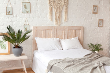 Big clean and light Scandinavian styled bedroom. Many flowers at home. Organic handmade macrame on the wall