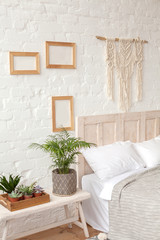 Scandinavian style bedroom in white and neutral colors. Handmade macrame and wooden frames mockup on the wall