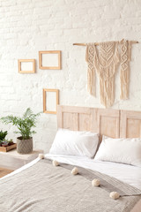 Scandinavian style bedroom in white and neutral colors. Handmade macrame on the white brick wall. Organic and eco friendly living