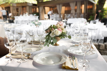Fototapeta na wymiar Wedding table setting decorated with fresh flowers in a brass vase. Wedding floristry. Banquet table for guests outdoors with a view of green nature. Bouquet with roses, eustoma and eucalyptus leaves