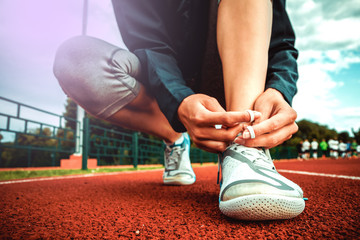 She is tying shoelaces. Athlete girl at a stadium. Concept of fitness and sport.