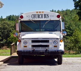 A White Church Bus Parked in Front of Trees