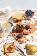 Appetizing toasts with chocolate paste, coffee with milk, figs and blueberries on the table.
