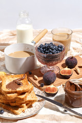 Appetizing toasts with chocolate paste, coffee with milk, figs and blueberries on the table.