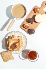 Appetizing toasts with chocolate paste, coffee with milk, figs and blueberries on the table.