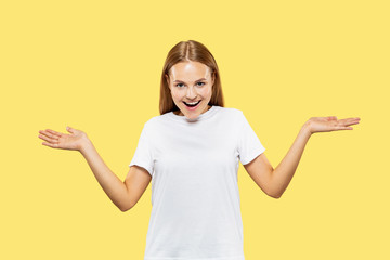 Caucasian young woman's half-length portrait on yellow studio background. Beautiful female model in white shirt. Concept of human emotions, facial expression. Showing an empty bar and smiling.