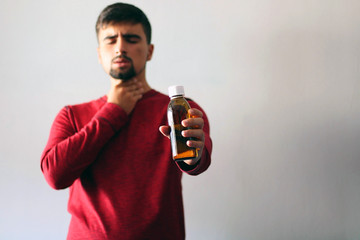 Health and Medicine Concept: Young boy cold dressed in red holding a cough syrup.