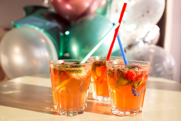 Citrus crushed ice cold refreshing cocktail with mint. Glass of strawberry soda drink on the background of balloons. Selective focus. Top view. Summer concept.