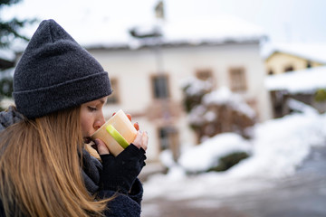 Young happy girl drinking a hot cup of tea with a snowy background during a cold winter day