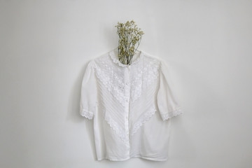 Vintage white lace blouse and gypsophila flowers, hanging on a white wall.