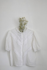 Vintage white lace blouse and gypsophila flowers, hanging on a white wall.