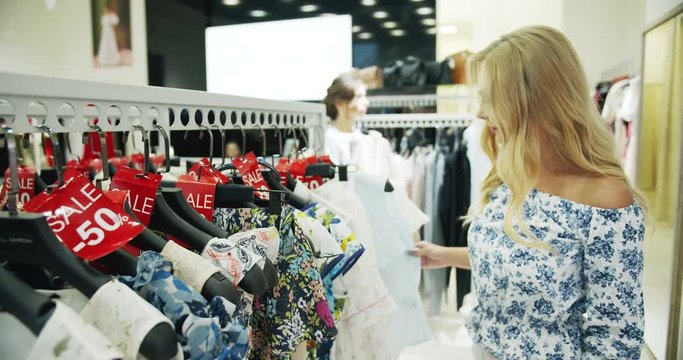 Attractive blonde woman looking through clothing in shop, reasonable discounts, shopaholics
