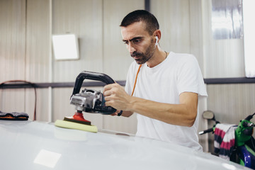Car detailing - Hands with orbital polisher in auto repair shop. Selective focus.