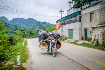 Une femme avec un masque contre la pollution transporte un imposant chargement sur sa moto, Vietnam.