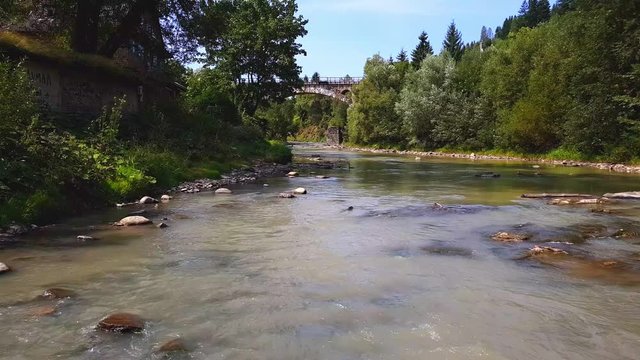 The train passes through a stone musta above the mountain, a shallow river with a fast current in the Carpathian mountains with a rocky bottom on a sunny day. 4K shooting