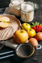 Autumn apple pie. Ingredients and cooking. Apples, eggs, flour, sugar. On a dark wooden background, close-up