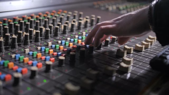 Close up of digital audio workstation with mixing console. Hand of record producer working on professional audio console with faders, scrolls weel, mixing music in sound recording studio