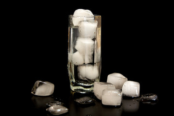 glass with ice on a black background. melting ice around splashing drops