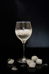 glass with ice on a black background. melting ice around splashing drops