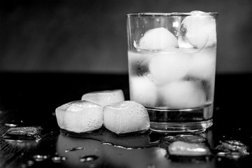 glass with ice on a black background. melting ice around splashing drops