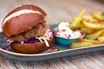 Pulled pork burger on a oval plate with french fries and mayonnaise dressing.